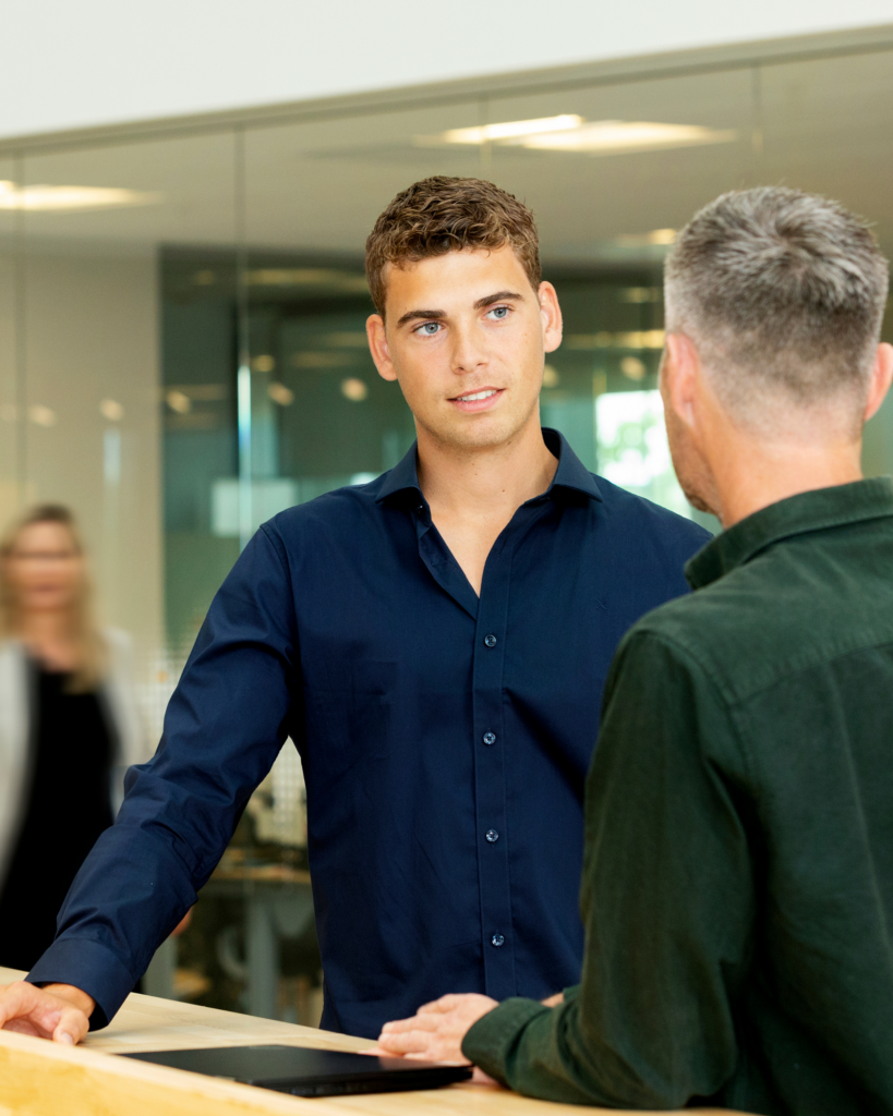 Dreng i mørkeblå skjorte og brunt hår kigger på og snakker med en mand, som man kun kan se bagfra
