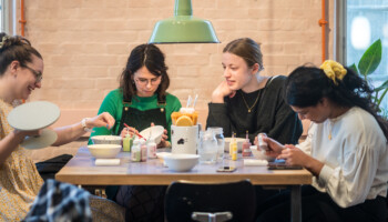 unge sidder rundt om et bord og maler på keramik