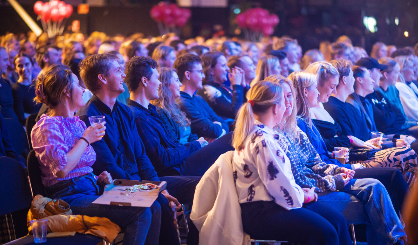 Fyldte publikumrækker med smilende og grinende folk