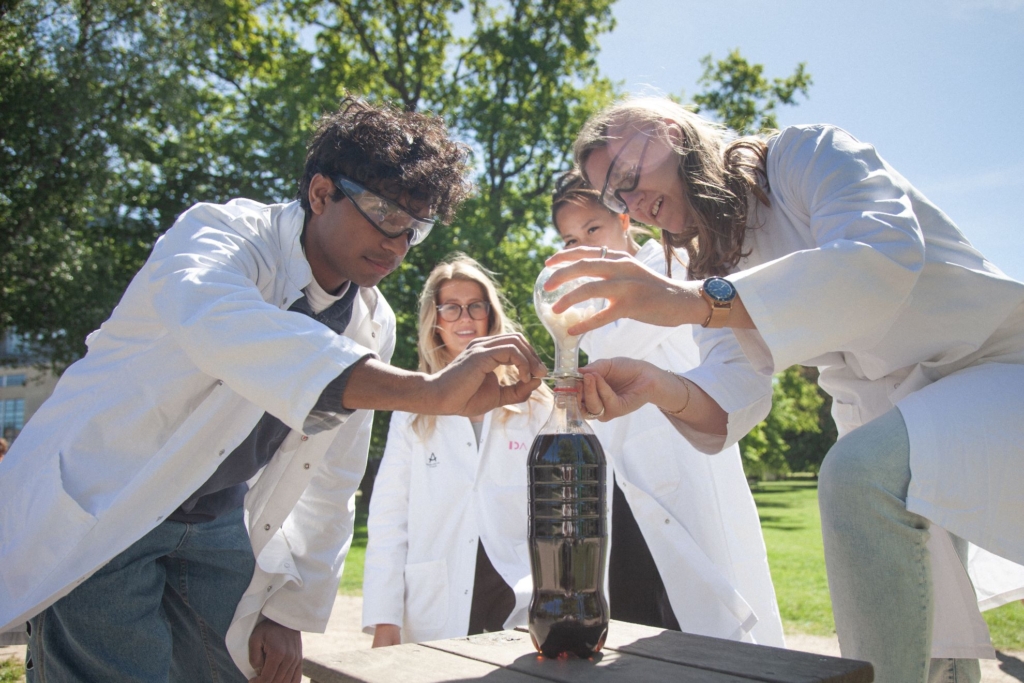 personer i laboratoriekitler foran et eksperiment med en flaske - de er udendørs