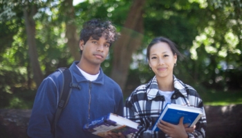 to personer kigger mod kameraet. de holder bøger. de står i grønne omgivelser.