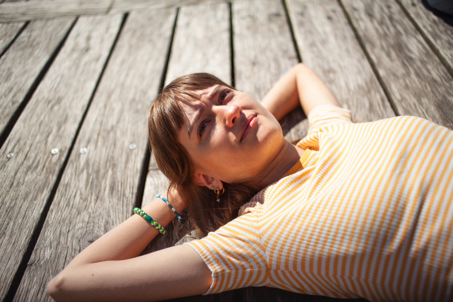 Pige med pandehår og stribet trøje ligger ned på en træbro og kigger op