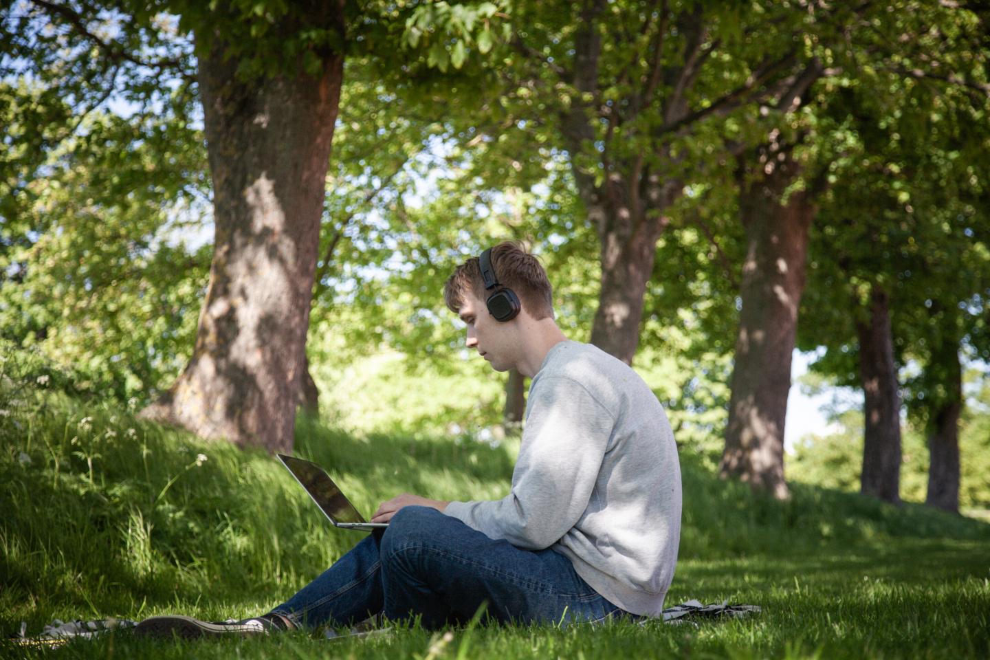 Mand sidder på græs, imens han sidder med sin laptop