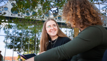 To kvinder sidder og snakker udenfor, imens den ene smiler.