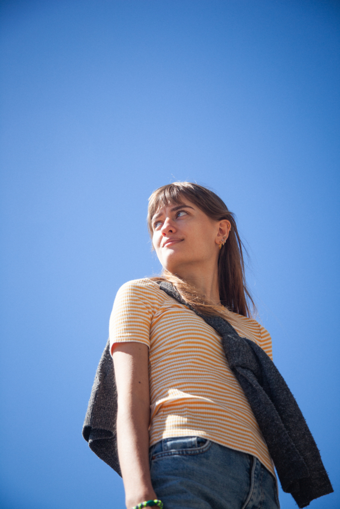 En pige står under blå himmel og smiler